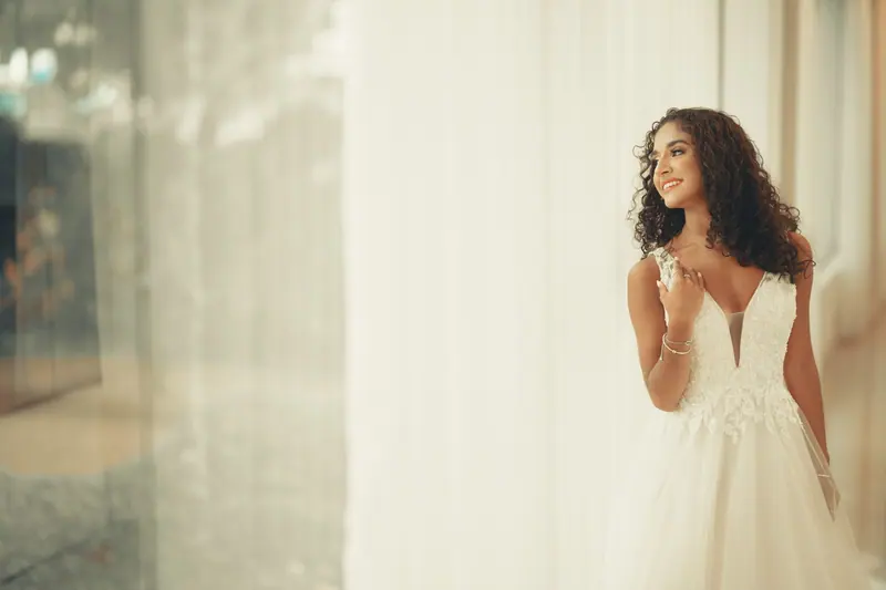 A beautiful young bride in a white dress, smiling indoors.