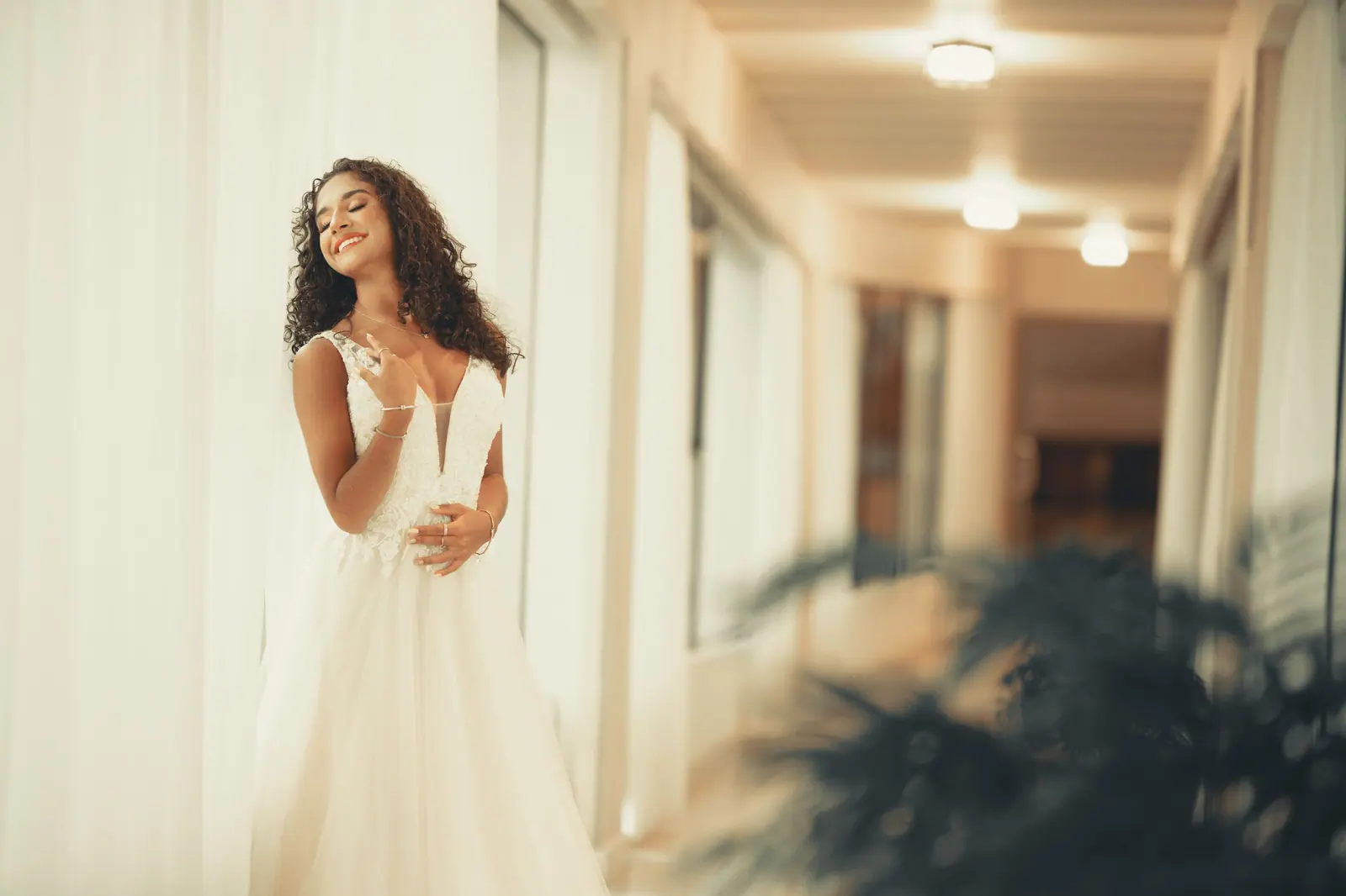 Portrait of a smiling woman in a white dress posing in an elegant indoor corridor.