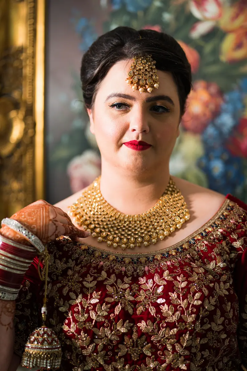 A woman in rich traditional attire poses with elegance against a floral backdrop, showcasing cultural beauty.