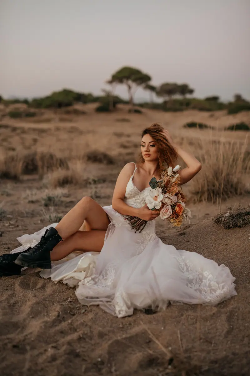 Elegant bride in rural setting holding bouquet, showcasing modern wedding fashion.