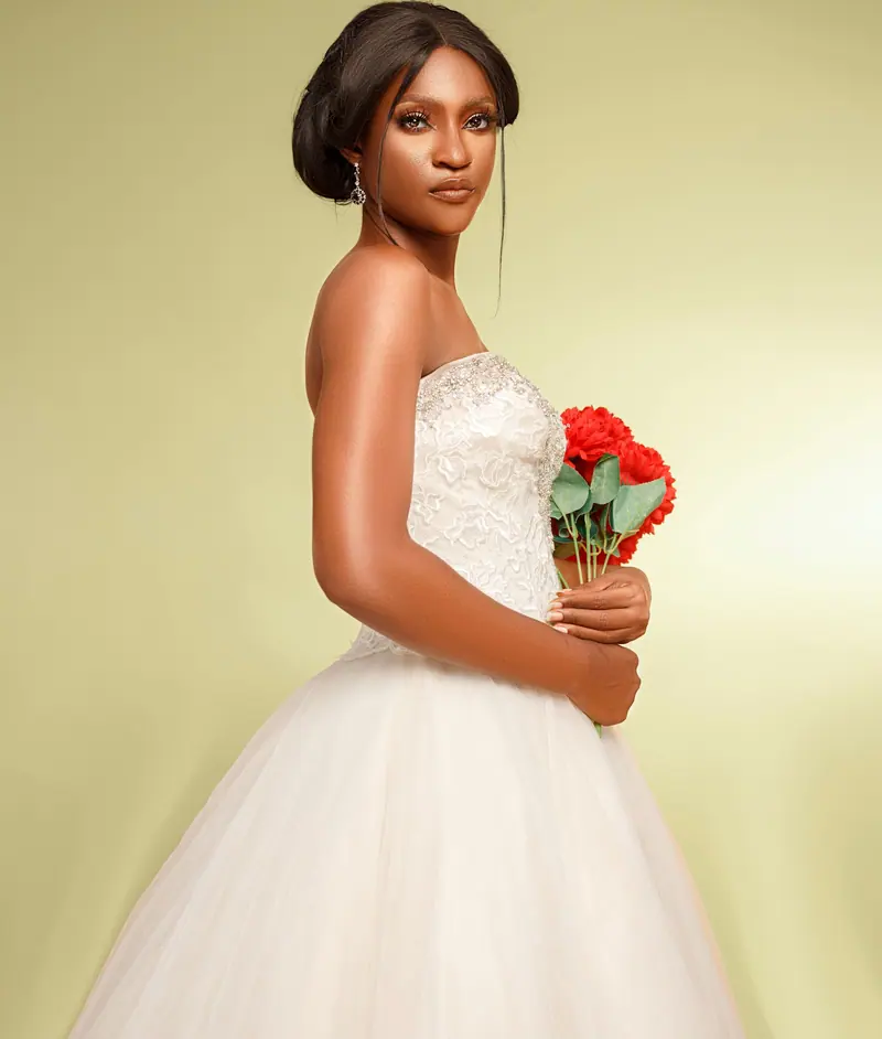Beautiful bride in a wedding dress holding a bouquet of red flowers against a yellow backdrop.