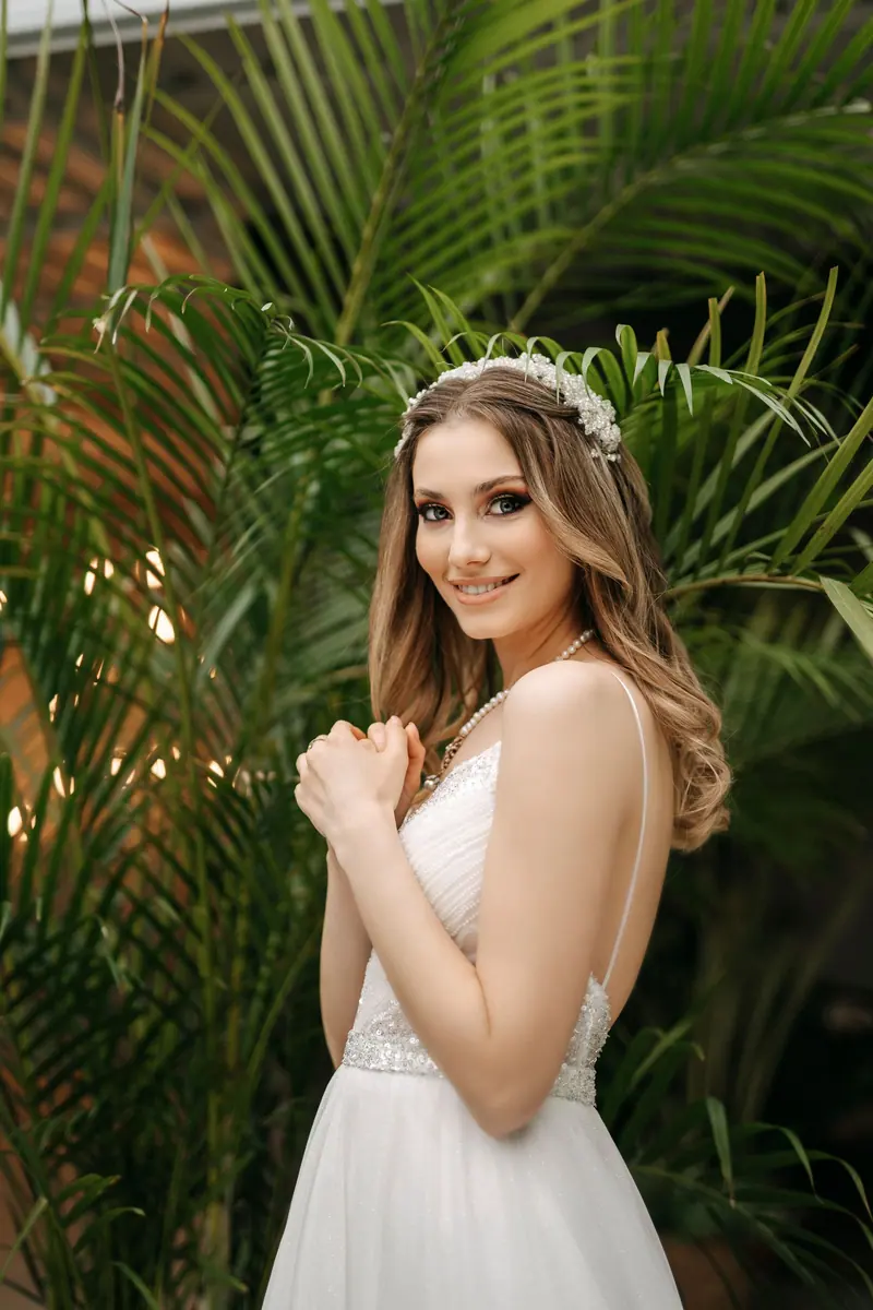 Charming bride in a white wedding dress smiles gracefully in a lush tropical backdrop.