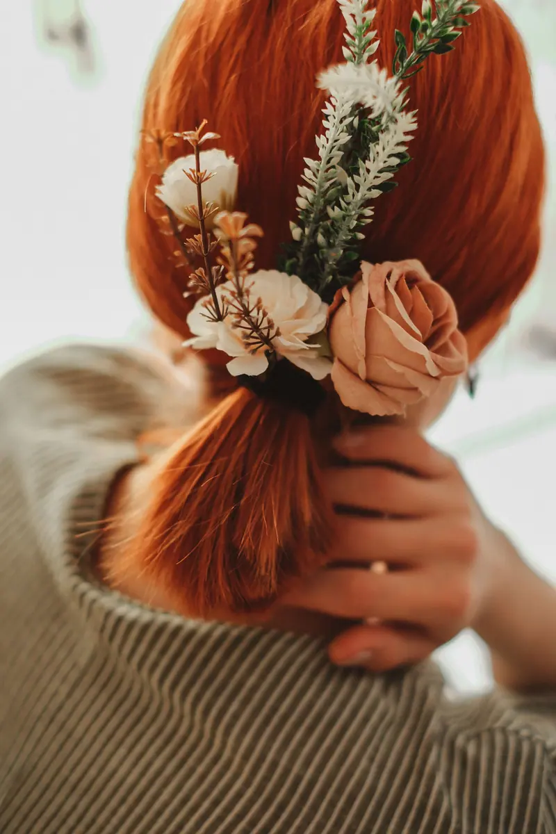 Close-up of redhead woman's ponytail with rustic floral hair accessories.