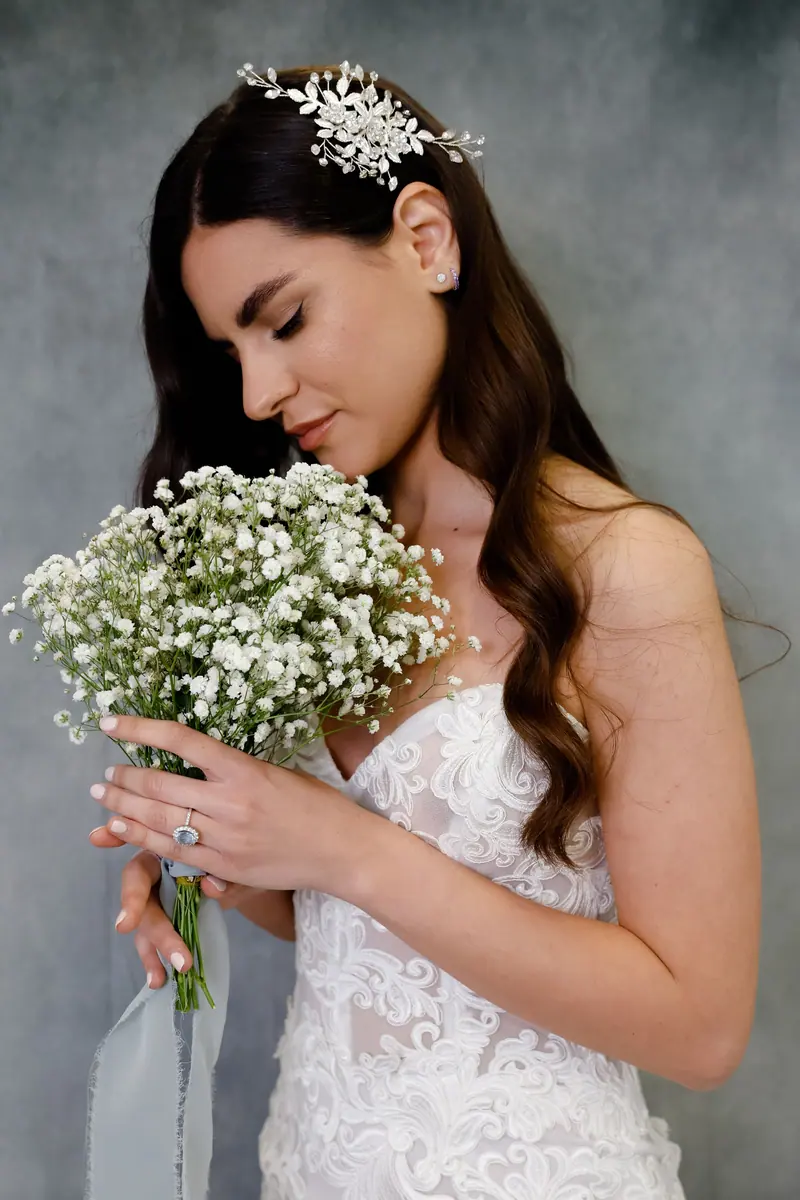 Beautiful bride in lace wedding dress holding a bouquet of white flowers against a gray background.