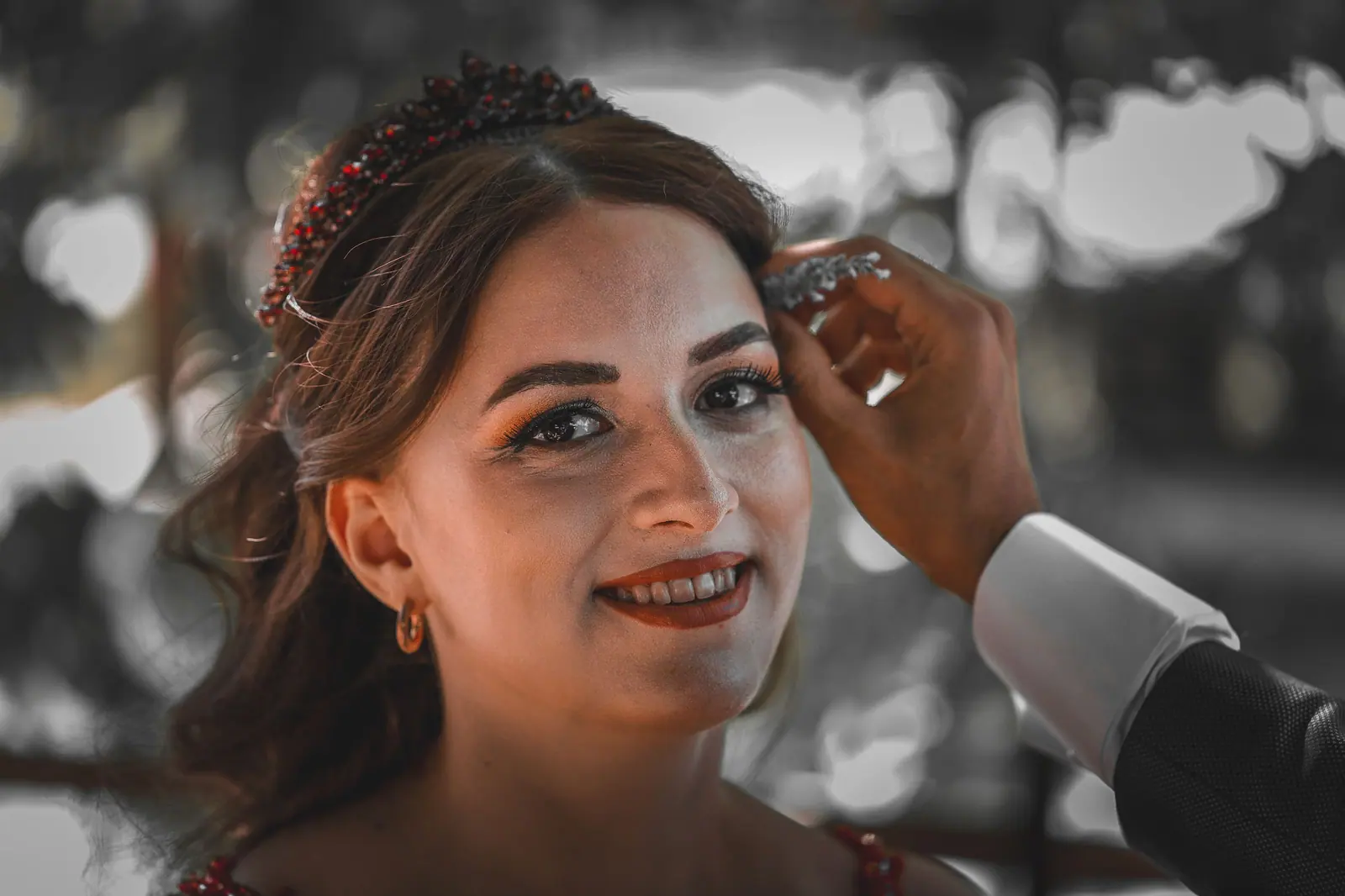 Close-up of a smiling bride being adorned with jewelry, showcasing an intimate wedding moment.