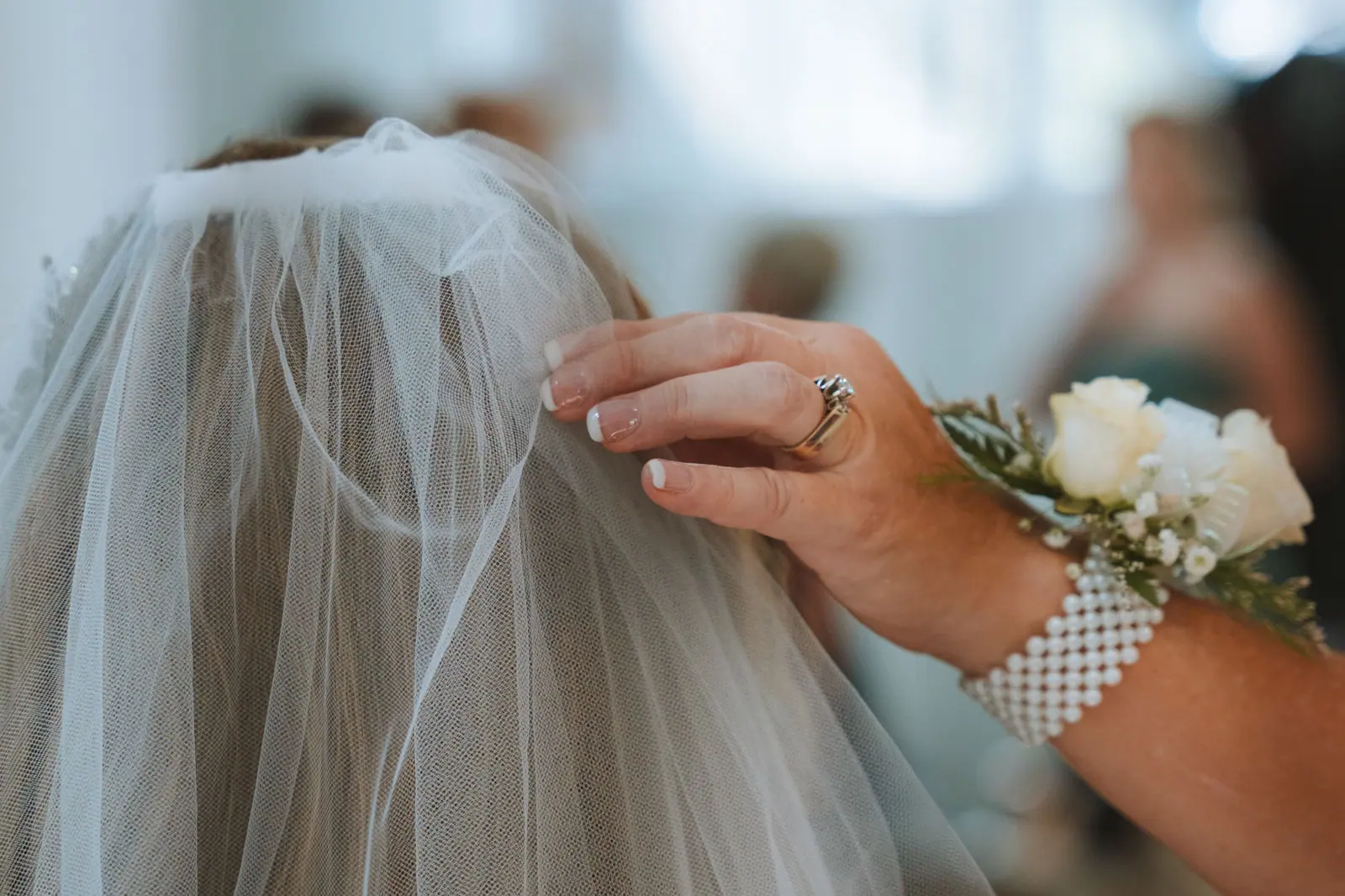 Detailed shot of a bride's veil being adjusted by a hand with floral decoration, capturing a tender wedding moment.