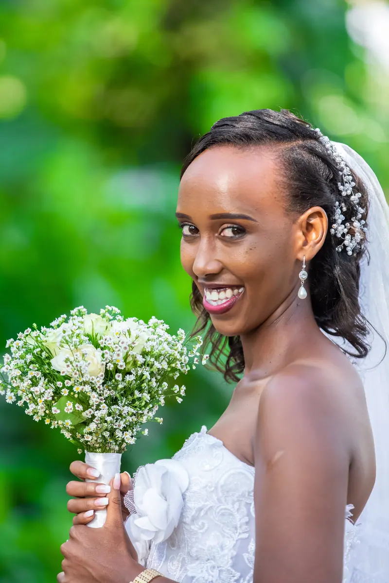 Radiant bride smiling holding floral bouquet in an outdoor setting.