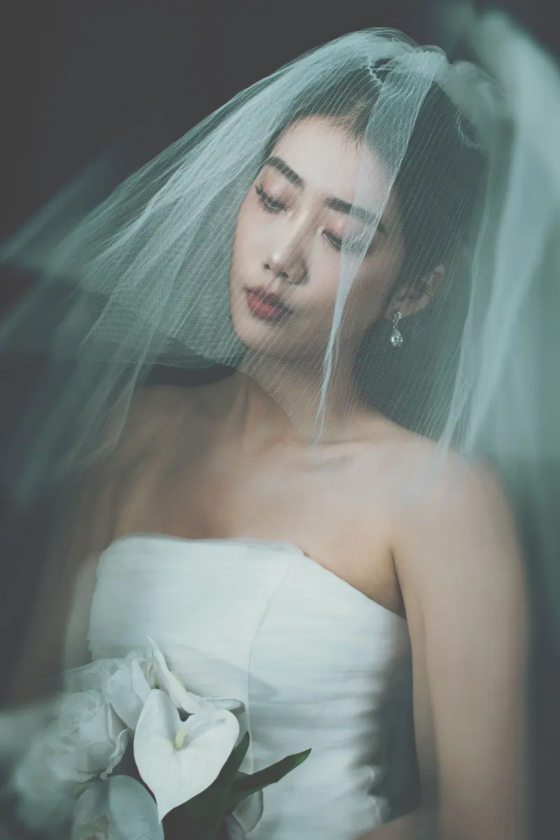Soft portrait of a bride in a strapless dress and veil holding white flowers.