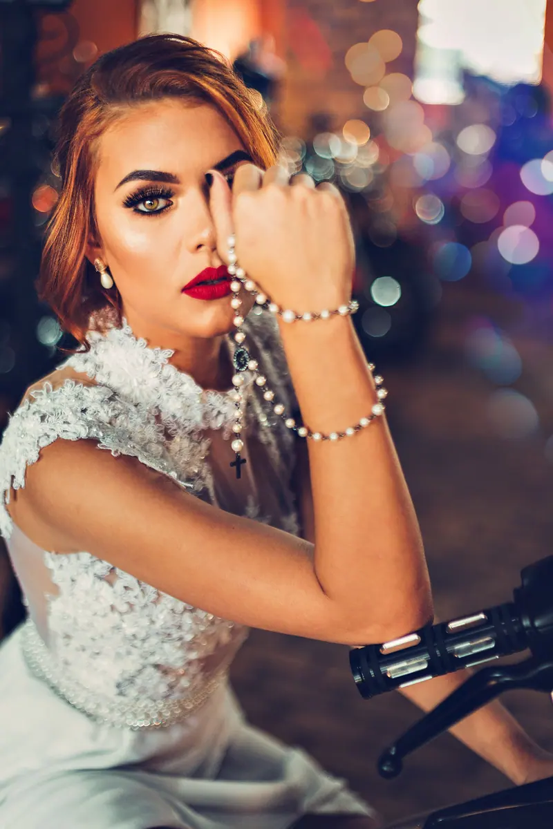 A stylish woman in a bridal dress holds a pearl necklace, exuding elegance and sophistication.