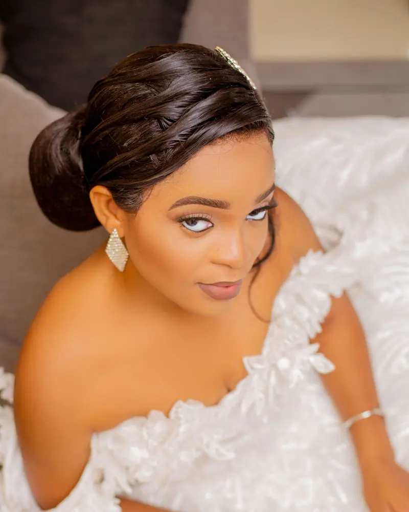 Beautiful bride in an elegant white wedding dress glancing upward, showcasing jewelry and hairstyle.