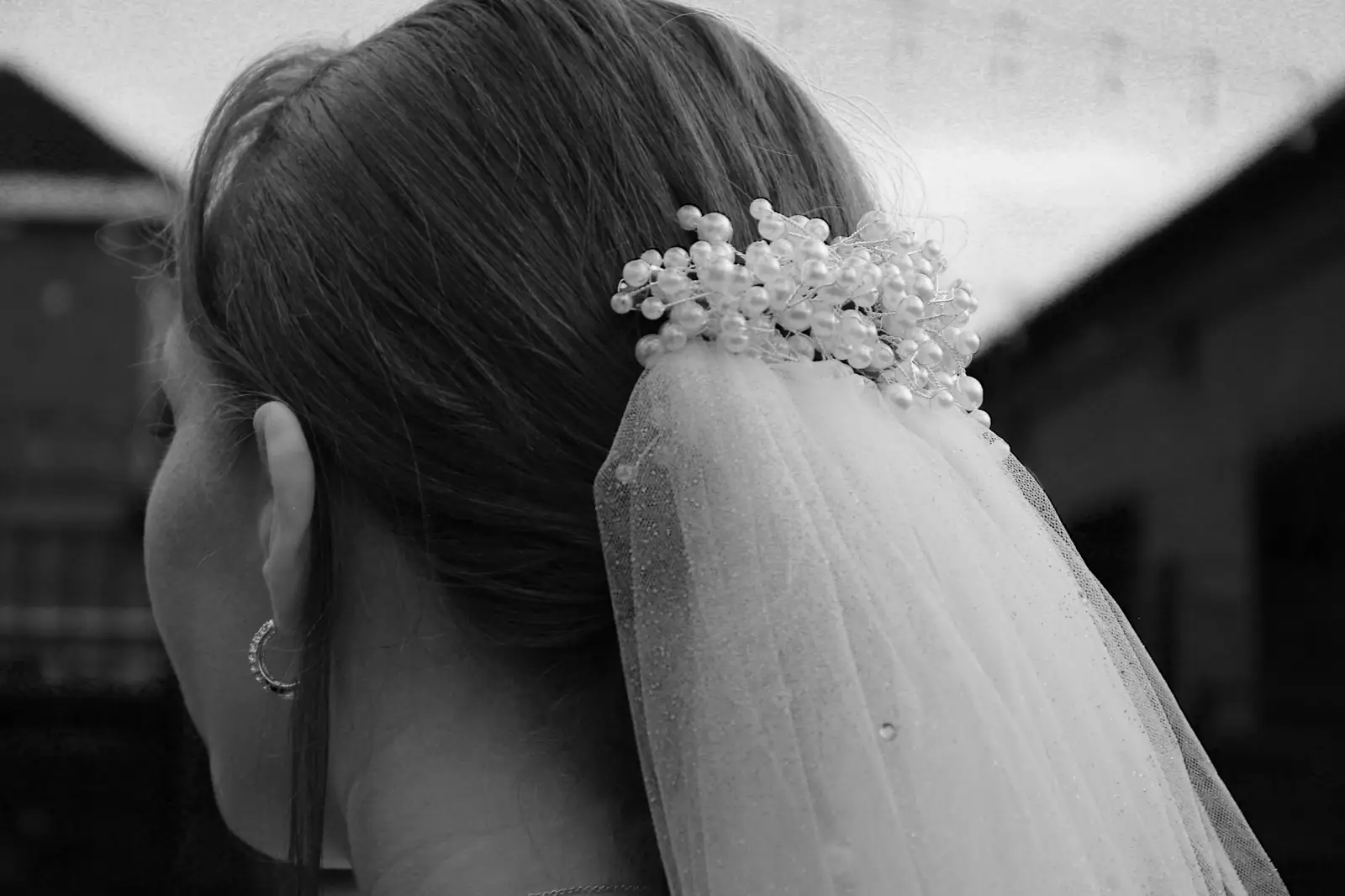 Black and white close-up of a pearl-studded veil pinned beneath a sleek bun