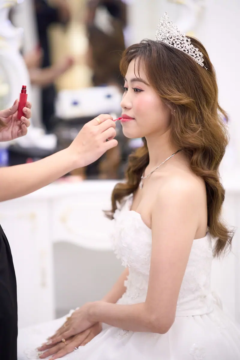 Beautiful Asian bride applying lipstick in a makeup room, preparing for her wedding day.
