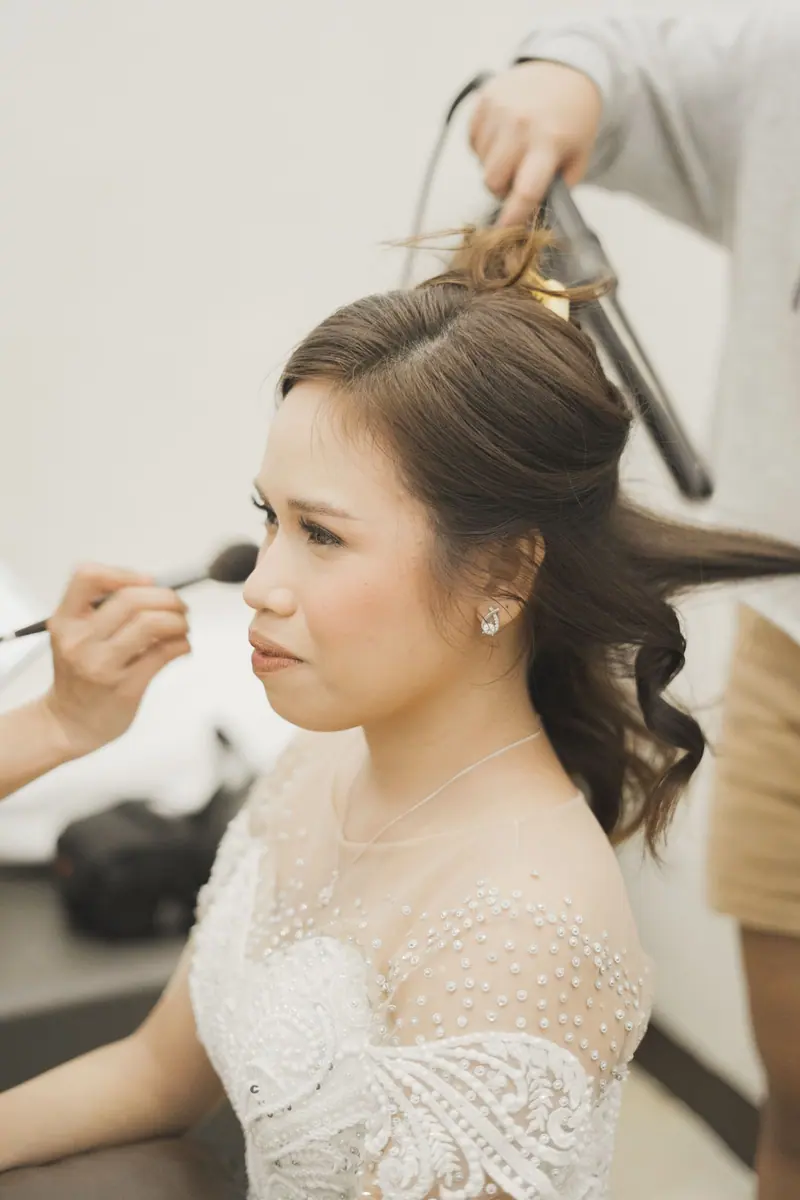 Bride receiving final touches of makeup and hair styling before wedding.