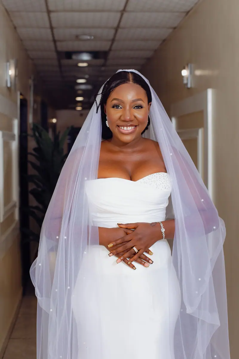 Elegant African bride in white wedding dress smiling brightly indoors, capturing happiness.