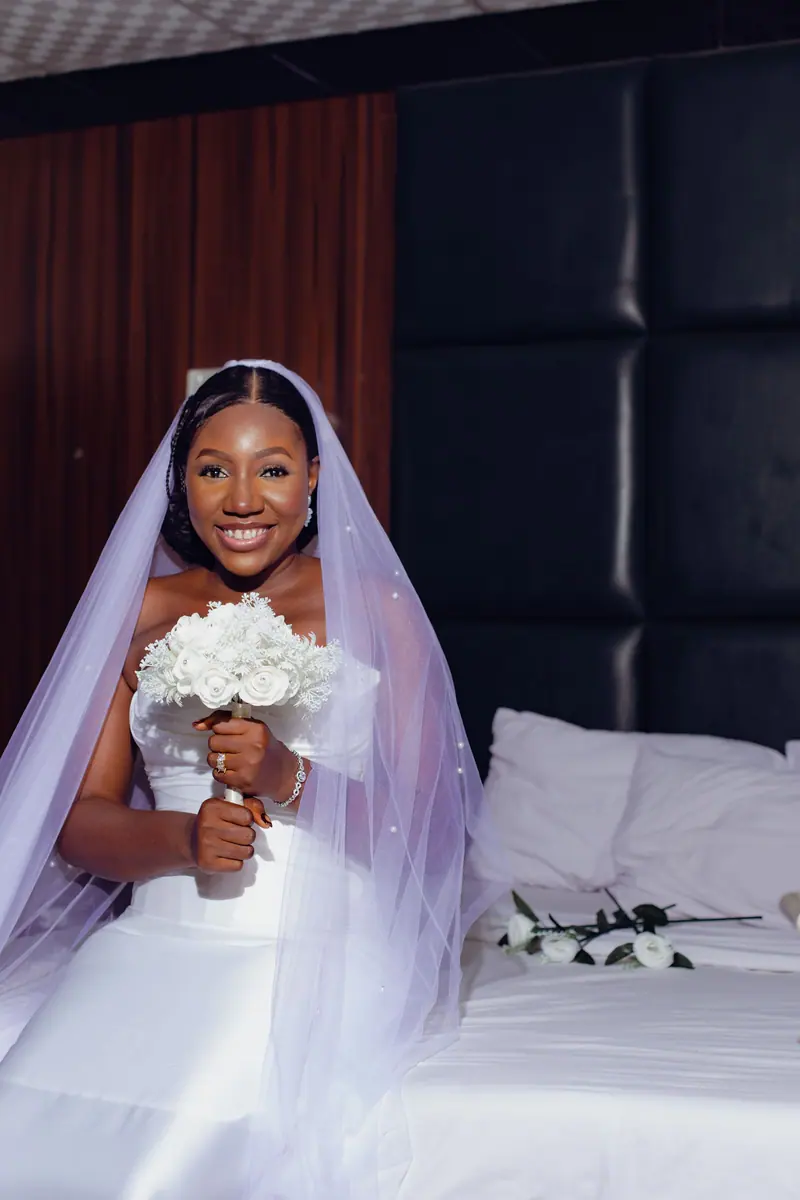 Stunning bride in wedding dress holding white bouquet, sitting with a joyful smile.