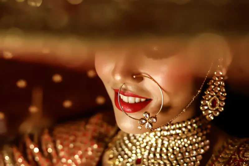 Close-up of a smiling Indian bride with intricate jewelry and red lipstick, showcasing traditional elegance.