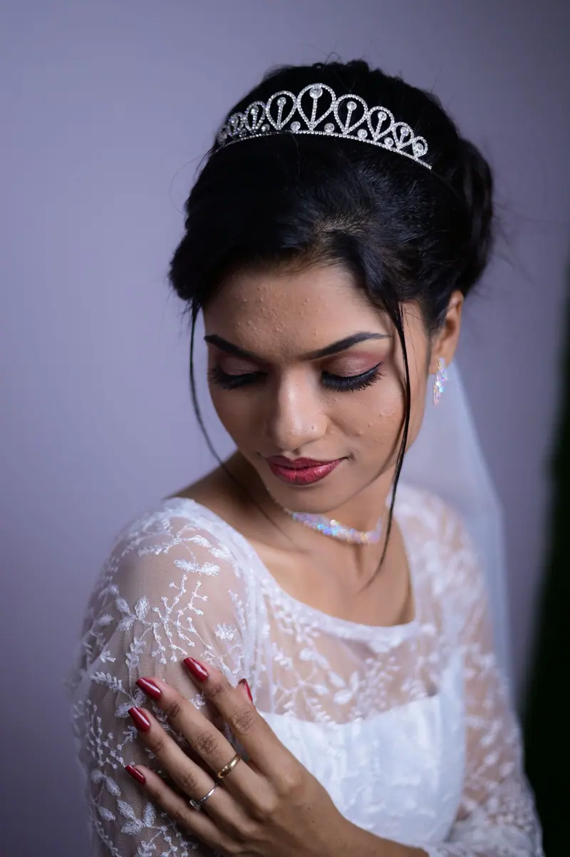 Elegant bride in a lace wedding dress and tiara poses gracefully in a studio setting.