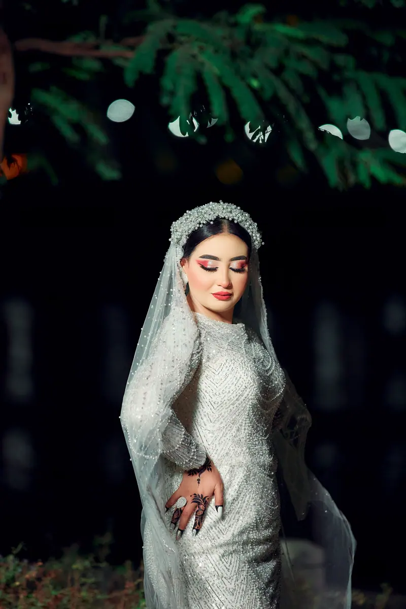 Beautiful bride in an elegant gown with intricate henna standing gracefully outdoors at night.