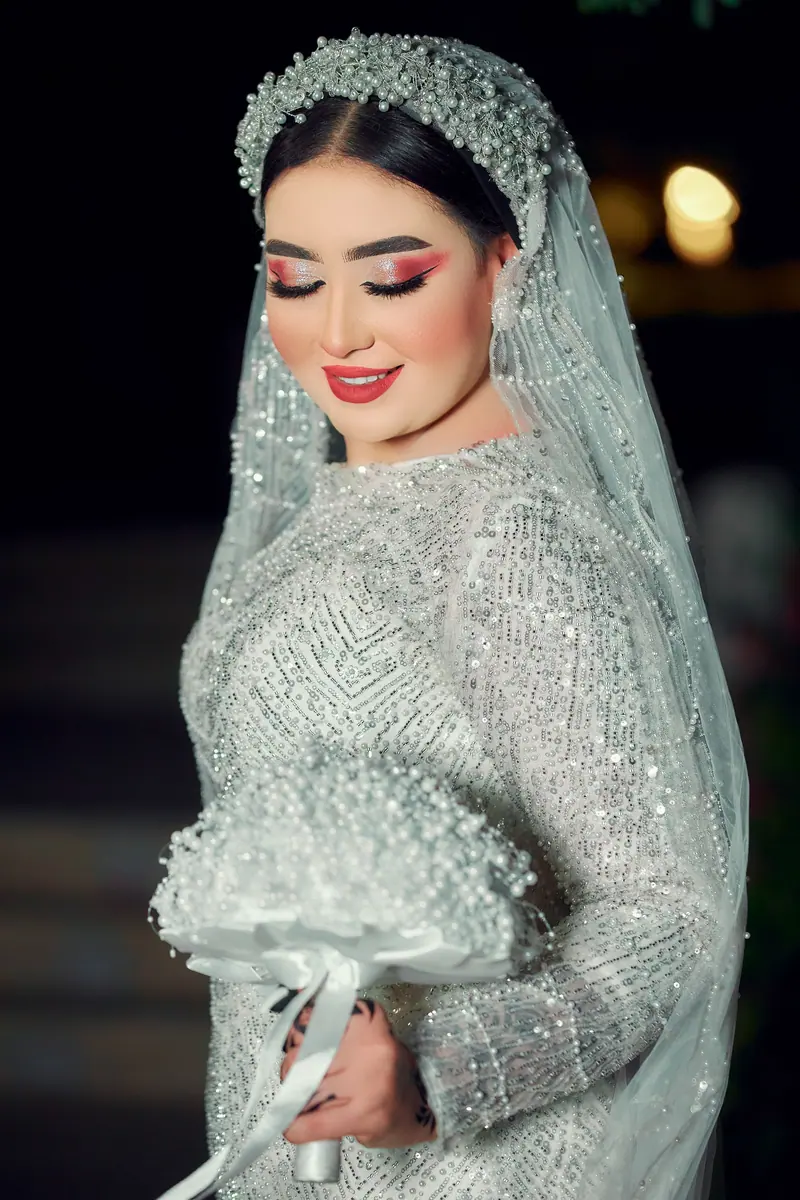 Beautiful bride in a glittering gown, holding bouquet, posing elegantly.