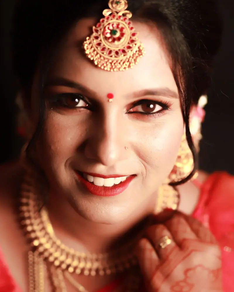Portrait of a smiling Indian bride in traditional attire and jewelry, captured indoors.