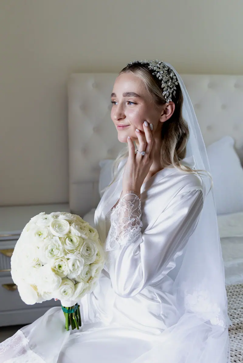 Beautiful bride in wedding dress with white rose bouquet, indoors setting.