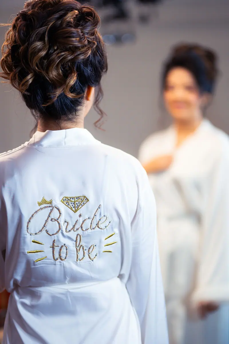 A woman wearing a 'Bride to Be' robe getting ready in the mirror.
