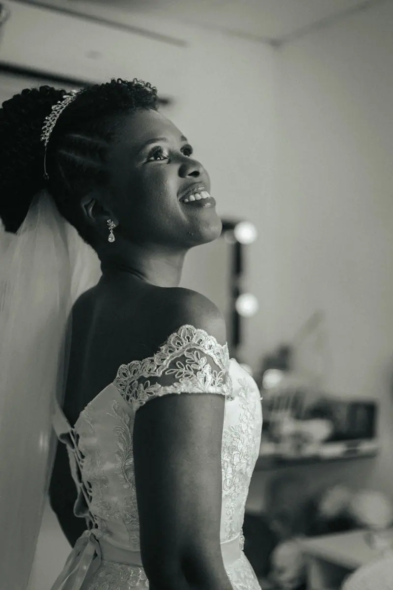 A joyful bride in a lace wedding dress captured in an elegant black and white portrait indoors.