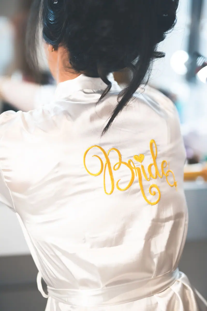 Back view of bride wearing a silk robe with 'Bride' embroidery in gold script.