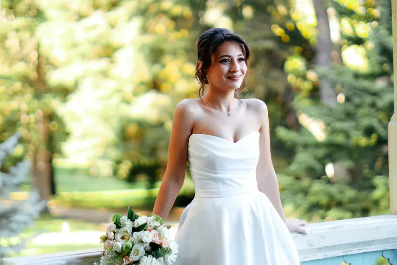 Beautiful bride standing in sunlight with floral bouquet, captured outdoors.