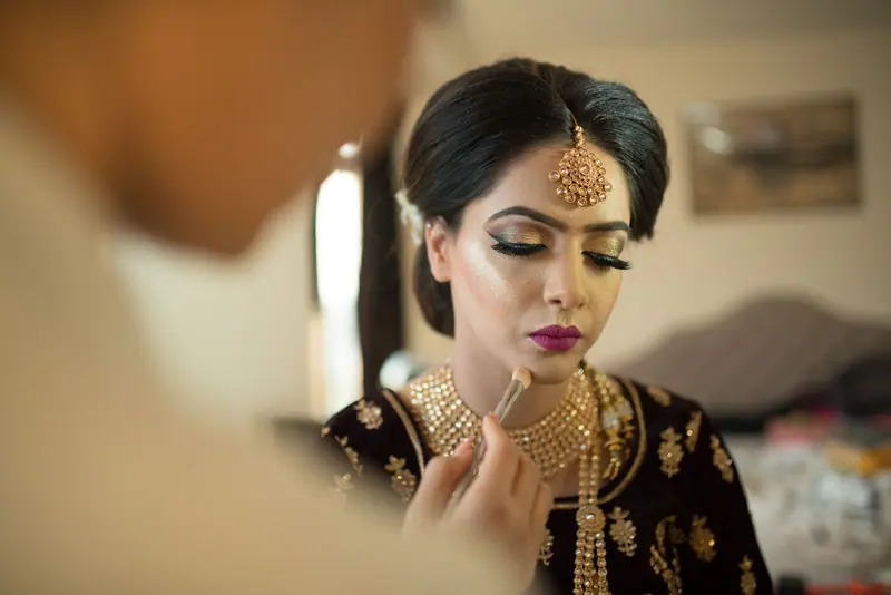 A bride getting her traditional makeup done, wearing elegant jewelry.