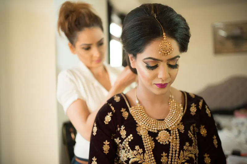 A bride getting ready in traditional attire and jewelry, assisted by a stylist.
