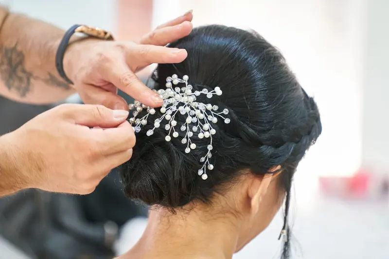 Photograph of a hairstylist arranging an elegant updo embellished with delicate decorative pins in a professional studio.