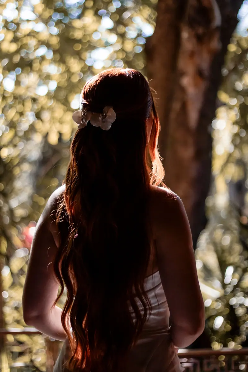 A woman with long red hair and floral hair accessories in a natural setting.