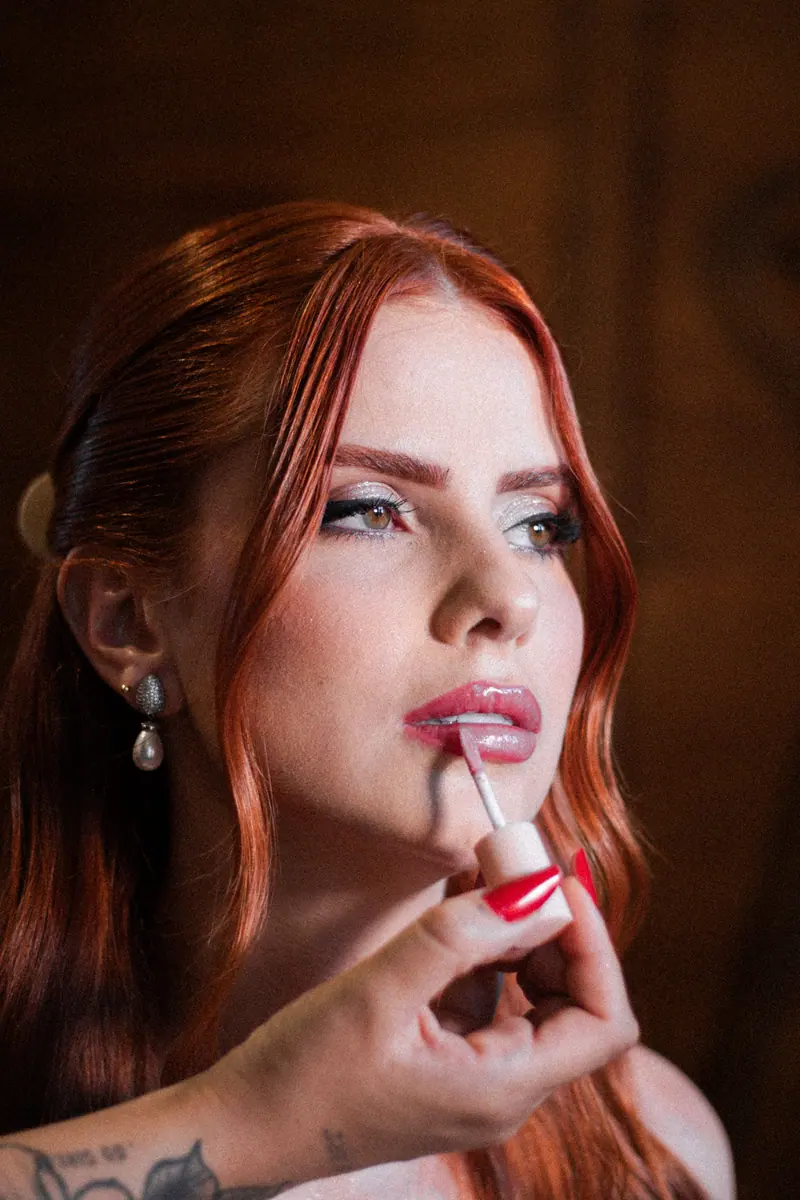 Close-up of a woman with red hair getting lip gloss applied, highlighting beauty and elegance.
