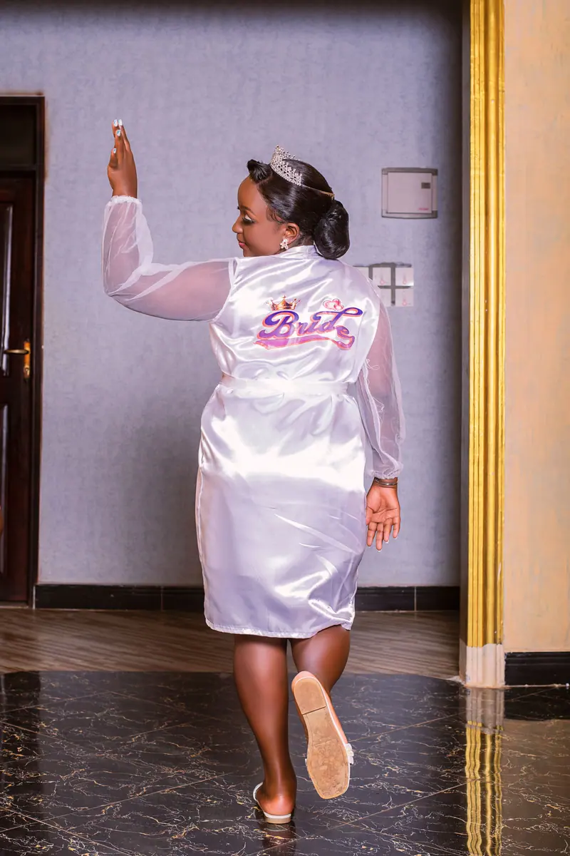 Bride in a satin robe and tiara joyfully preparing for her wedding day inside a stylish venue.