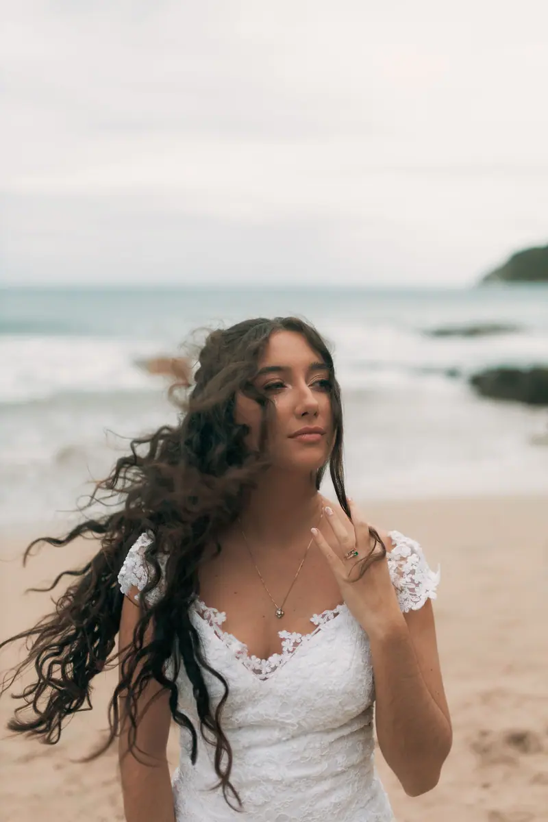 Bride in lace dress on sandy beach with waves and soft light ambiance.