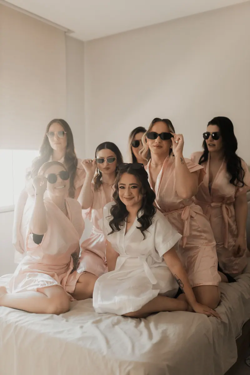 A joyful bridal party posing in matching robes and sunglasses, creating a fun and relaxed vibe indoors.