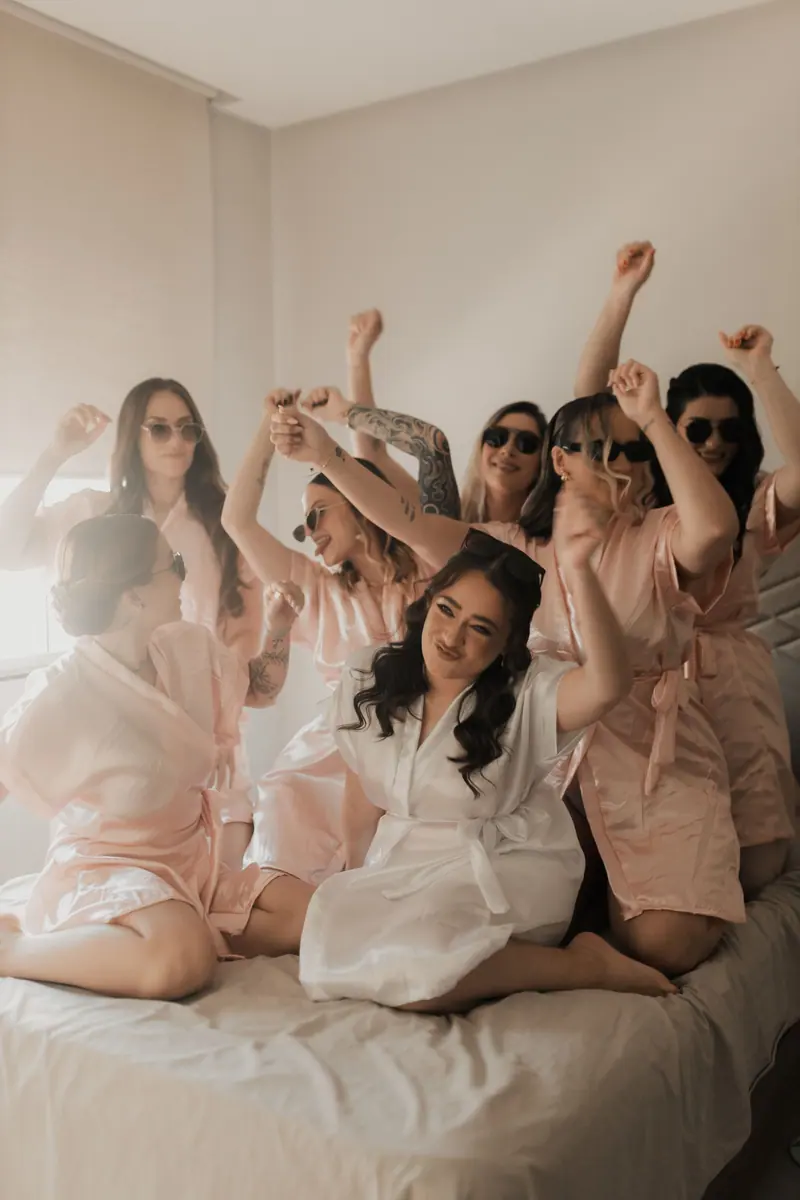 A joyful bridal party in satin robes celebrating on a bed indoors, creating a warm and fun atmosphere.