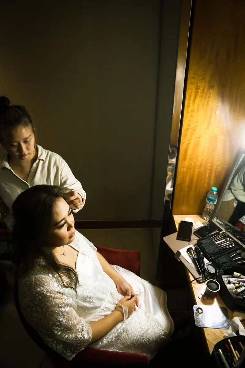 A bride getting her hair done by a stylist in a warmly lit room.