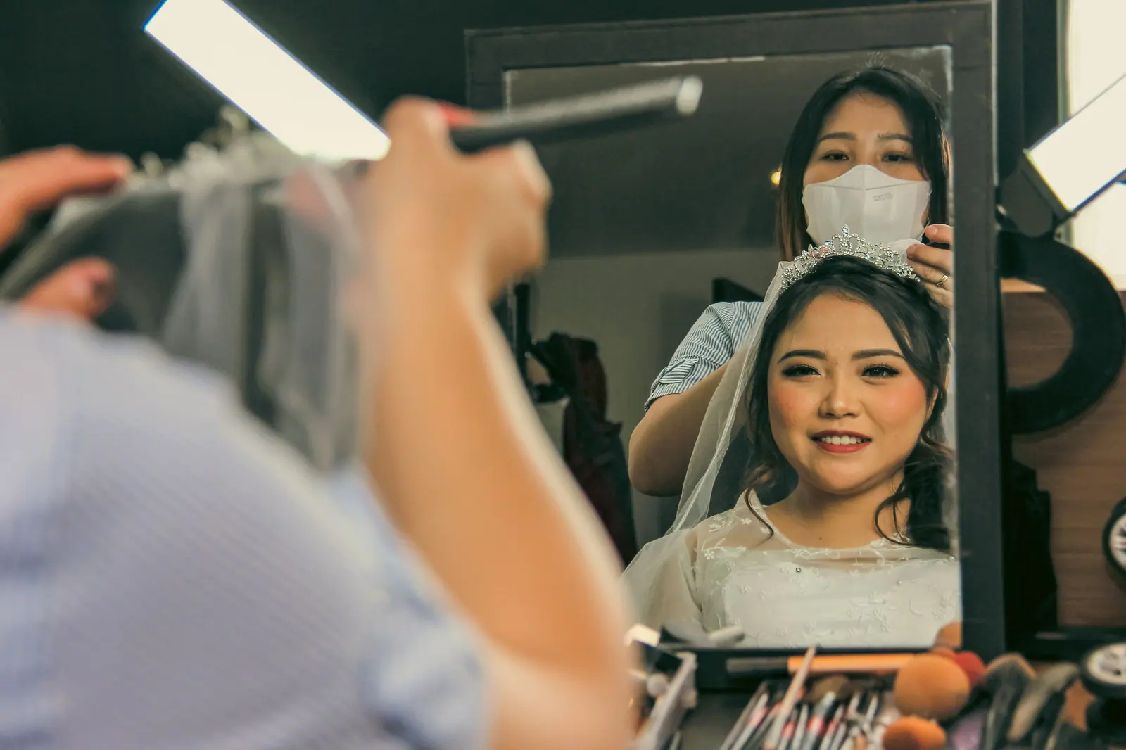 A bride being prepared by a hairstylist in a makeup studio, reflecting joy.