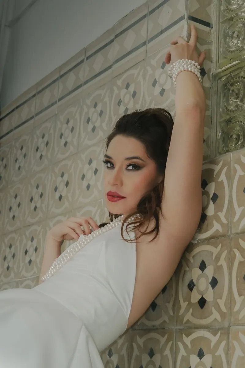 Stunning portrait of a woman in bridal attire adorned with pearls against tiled wall.