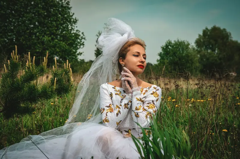 Bride in a white embroidered dress and veil enjoying nature in a lush green meadow.