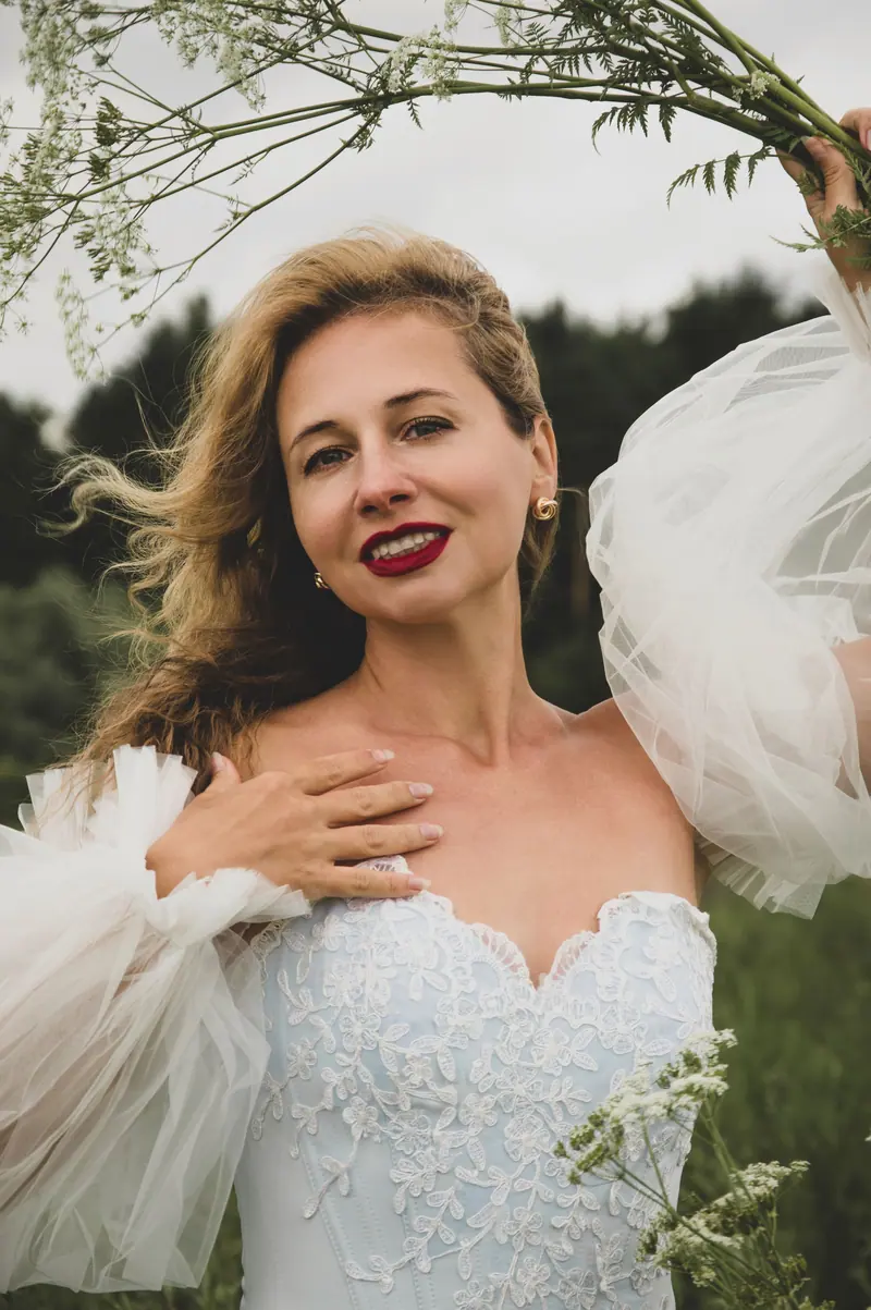 Elegant bride in white dress and flowers, outdoors with natural backdrop.