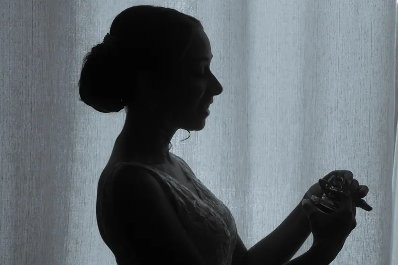 Silhouette of a bride in profile holding a perfume bottle in elegant pose.