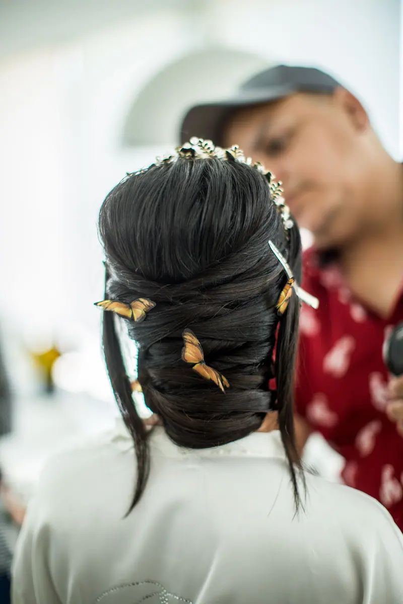 Rear view of a beautifully styled bridal hair with butterfly clips, set indoors with a hairstylist in the background.