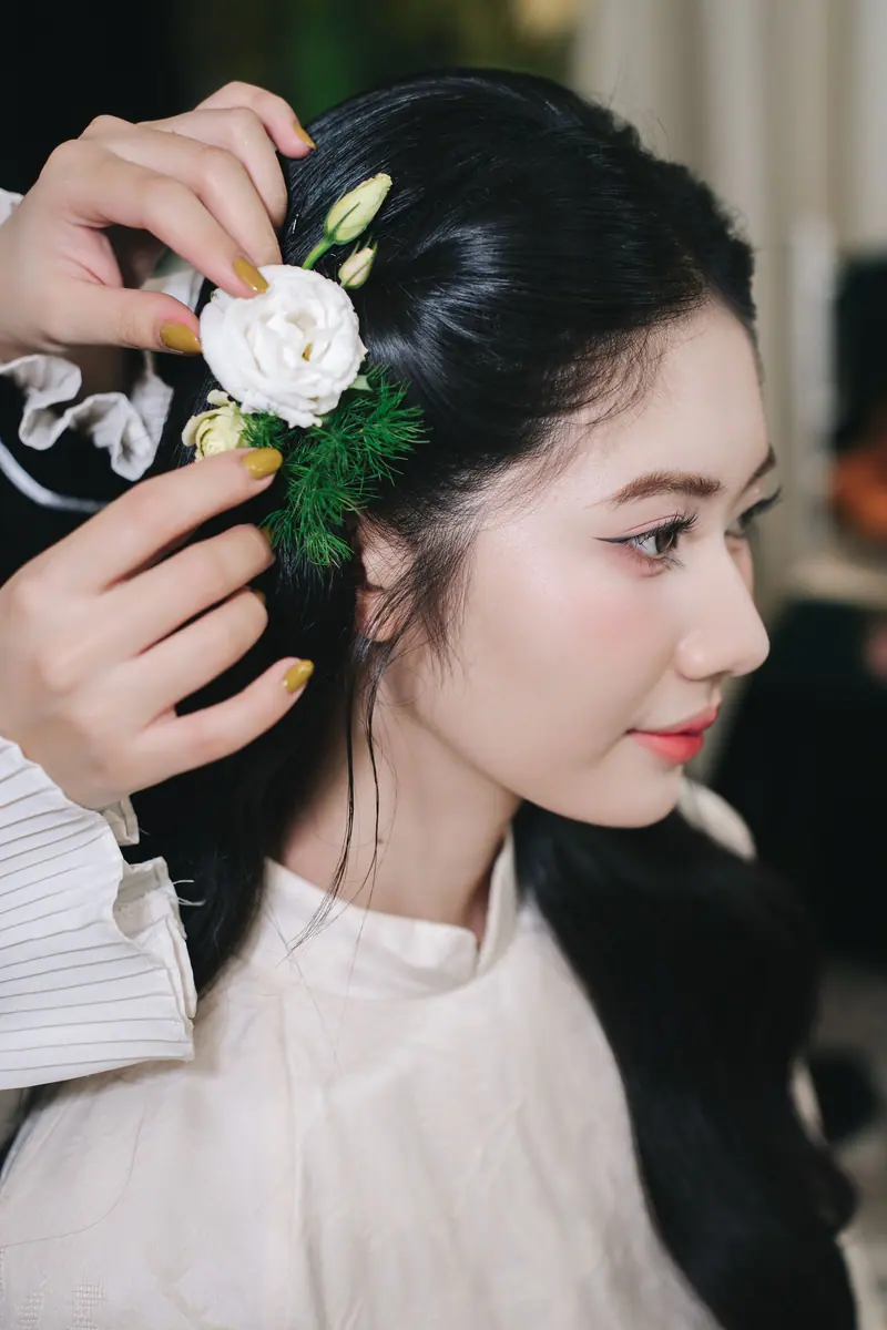 Close-up of a woman having a white floral accessory styled in her hair indoors.