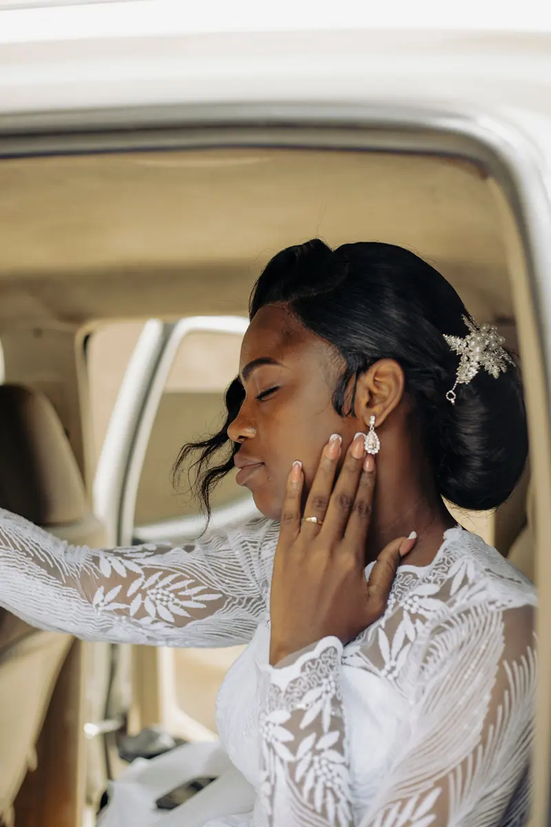 Beautiful bride in lace dress sitting inside a car, exuding elegance and grace.