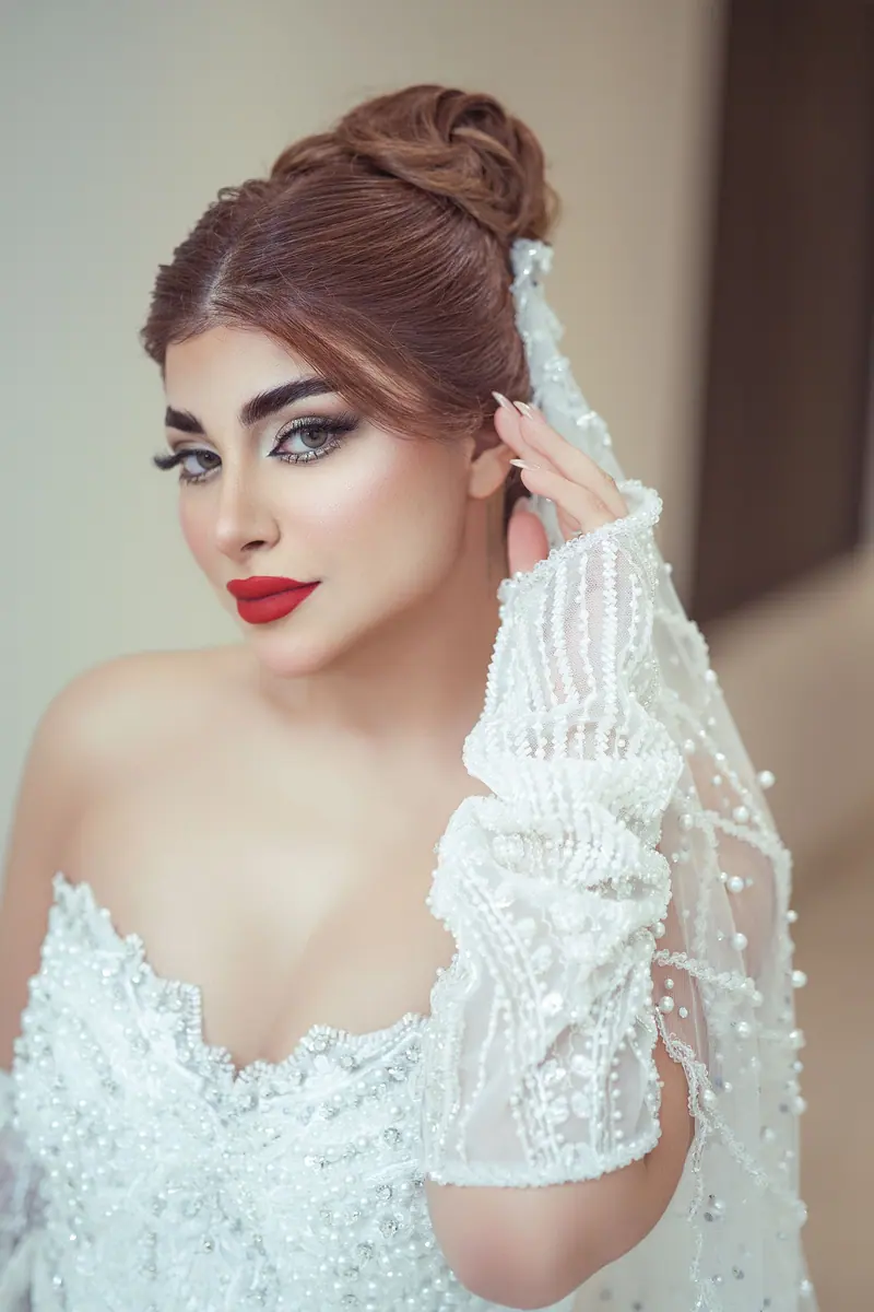 Beautiful bride in white gown with pearl details posing gracefully indoors.