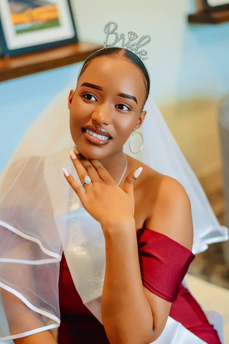 Beautiful bride in a red dress with a veil and tiara, smiling indoors.