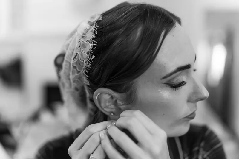 Elegant black and white portrait of a bride adjusting her earring while preparing for her wedding.